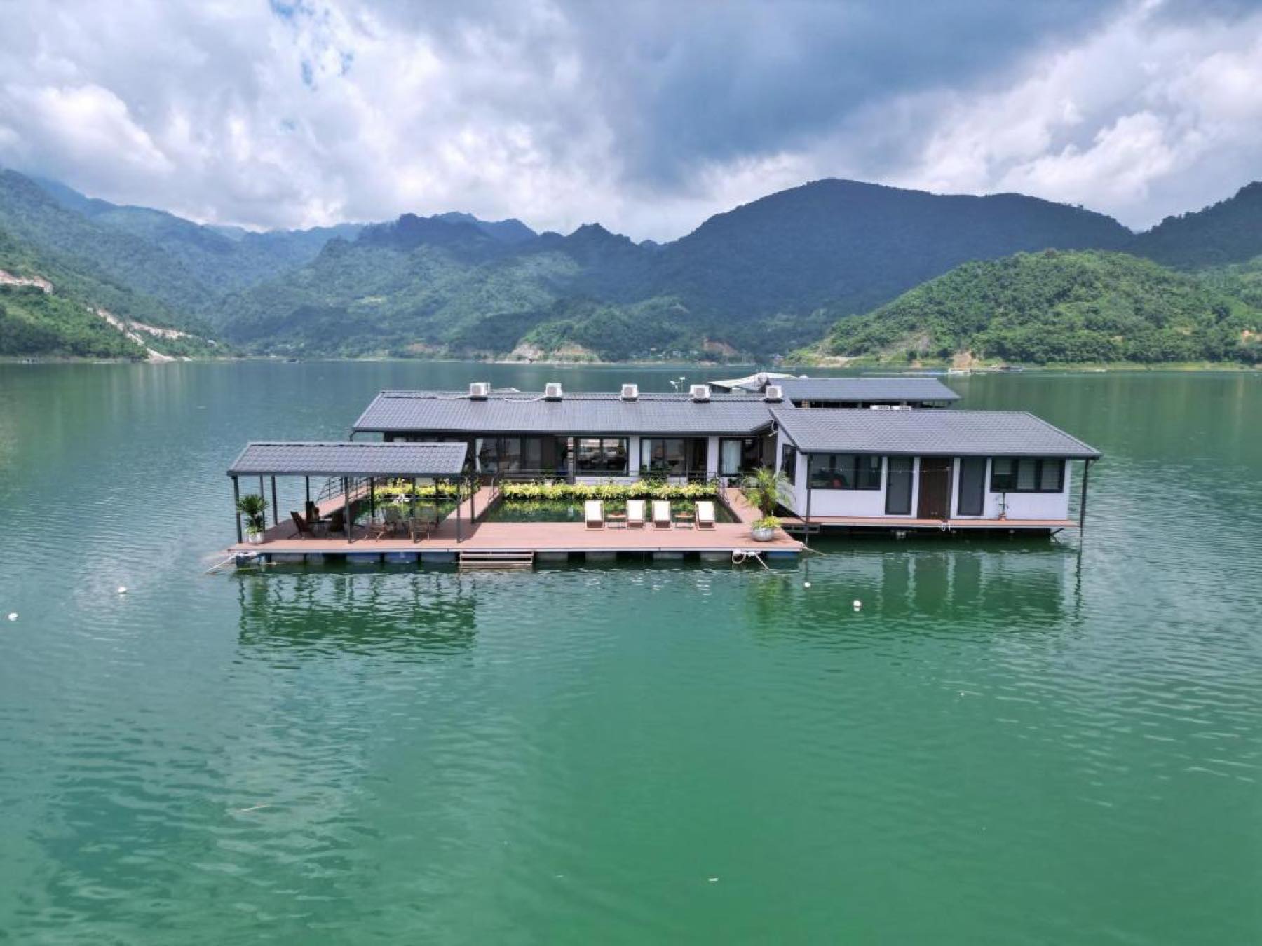 The Go Beyond floating lake house moored on Hoa Binh lake, northern Vietnam, with forested mountains behind.