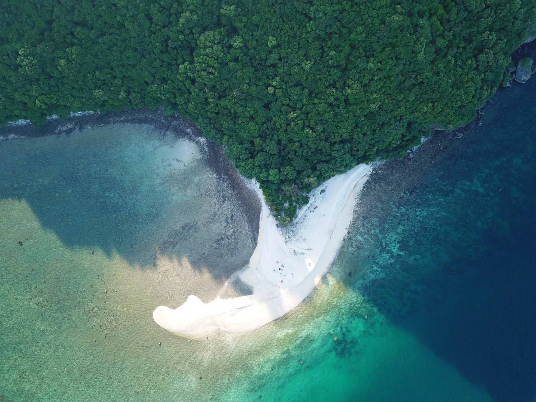 Aerial view of Koh Kye, a jungle-covered island ringed by a white coral sand spit and turquoise water.